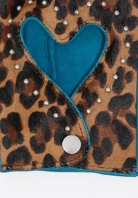 Accesorio de estampado de leopardo con un recorte en forma de corazón turquesa, adornado con tachuelas plateadas y acentuado con ribete azul. Superficie suave y texturizada.