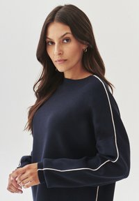Sweatshirt bleu marine avec col rond, manches longues et passepoil blanc contrastant le long des épaules, fabriqué en tissu tricot doux.