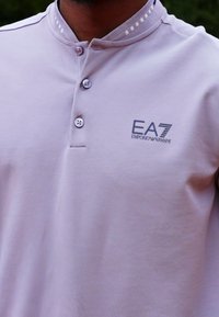 Světle fialová polo košile s třemi knoflíky, pruhovaným límečkem a logem EA7 Emporio Armani na levé hrudi. Hladká bavlněná textura.