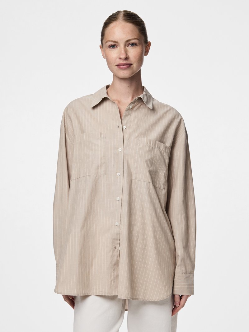 Šviesiai smėlio spalvos ilgomis rankovėmis marškiniai su vertikaliomis baltomis juostelėmis, smailiais antkakliais, sagomis priekinėje dalyje ir dviem krūtinės kišenėmis. Minkšta audinio tekstūra.