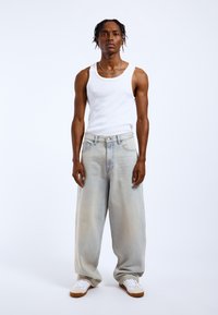 Jasnoniebieskie dżinsy o luźnym kroju, zestawione z białym topem na ramiączkach i białymi trampkami. Cechą charakterystyczną jest klasyczny pięciokieszeniowy fason.