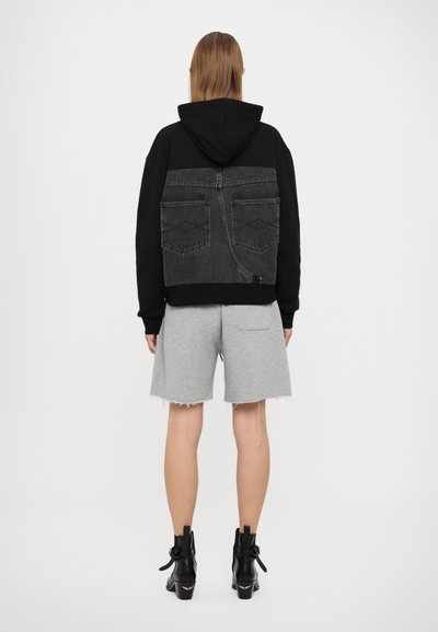 Hanorac negru cu glugă, cu spate din denim gri, având două buzunare și un design distinctiv al cusăturilor. Combinat cu pantaloni scurți gri și cizme negre până la glezne.