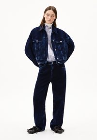 Giacca di velluto a coste blu navy con due tasche sul petto, abbinata a pantaloni larghi coordinati e mocassini neri con frange. Tessuto testurizzato.