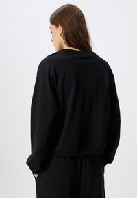 Zwarte cropped sweatshirt met geribde manchetten en zoom. Suède-achtige textuur, losse pasvorm en verlaagde schouders voor comfort.