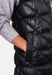 Hand in pocket of black quilted leather vest, with grey knit sweater sleeve visible.