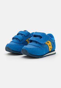 Blå sko laget av semsket skinn og nylon, med borrelåsremmer, en gul aksent med hull, og en teksturert gummisåle for grep.