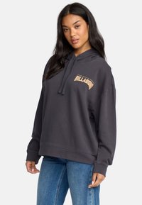 Sudadera de color carbón con un bolsillo canguro y un logo de Billabong texturizado en dorado. Corte relajado, tejido suave y puños acanalados.