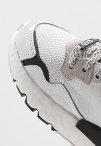 Baskets légères avec un dessus en maille gris texturé, des superpositions blanches brillantes, un accent en suède gris et une semelle striée noire.