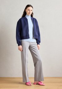 Navy bomber jacket, light blue turtleneck, gray wide-leg trousers, and pink sandals. Smooth fabric, gold zipper, and relaxed fit.