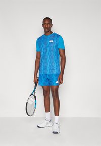 Blue athletic outfit featuring a patterned short-sleeve top and matching shorts. Includes a tennis racquet and white athletic shoes.