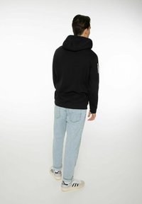 Felpa nera con un grande cappuccio, polsini e vita a coste. Abbinala a jeans blu chiaro e scarpe da ginnastica bianche con strisce nere.