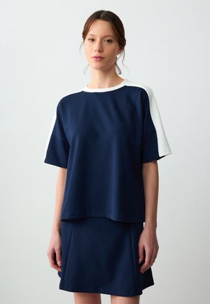 Top casual blu navy con dettagli bianchi sulle spalle, maniche corte e vestibilità ampia, abbinato a una gonna slim coordinata. Texture morbida.