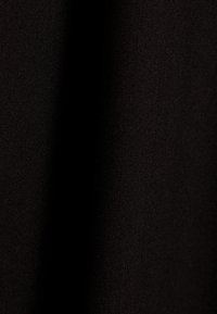 Gros plan sur un tissu noir avec une texture de tissage visible et des plis subtils créant des variations d'ombre.