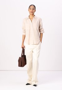 Light beige linen button-up shirt with two chest pockets, paired with high-waisted white trousers and a brown leather tote bag.