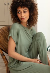 Olijfgroen loungewear set, met een losse top met opgerolde mouwen en brede, relaxte broek. Glad, zacht materiaal met een minimale textuur.
