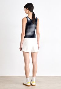 Striped tank top in navy and white, paired with cream shorts. Accessories include white sneakers with yellow accents and matching socks.