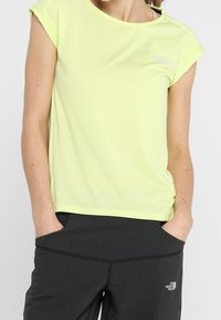 Lichtgele sporttop gemaakt van vochtregulerende stof, met korte mouwen en een ronde hals, gecombineerd met donkergrijze broek.