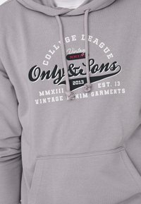 Sudadera gris con bolsillo frontal, capucha ajustable y estampado gráfico que presenta "Only & Sons" y otro texto en colores que contrastan.