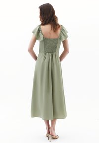 Zielona midi sukienka z krótkimi falbaniastymi rękawami, marszczonym tyłem oraz zwiewnym dołem. Gładki materiał i prosty, jednolity kolor.