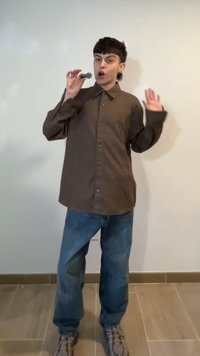 Νέος άνθρωπος που φοράει ένα καφέ πουκάμισο και τζιν κρατά με το ένα χέρι ένα μικρό μικρόφωνο κοντά στο στόμα του, ενώ το άλλο χέρι είναι σηκωμένο.