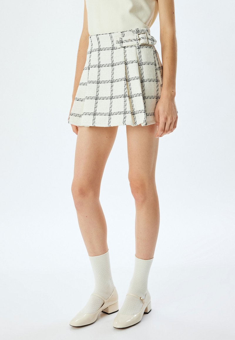 Witte geruite rok met zwart rasterpatroon, met een geplooide ontwerp en riemdetail; gecombineerd met crèmekleurige sokken en laarzen van patenleer.