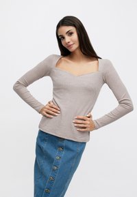 Μπεζ ριμπ πλεκτό τοπ με μακριά μανίκια και τετράγωνο λαιμόκοψη, σε συνδυασμό με μπλε τζιν pencil φούστα με κουμπιά μπροστά.