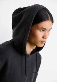 Black hoodie with a textured finish, drawstring hood, and front pocket. Features a subtle logo on the chest and casual fit.