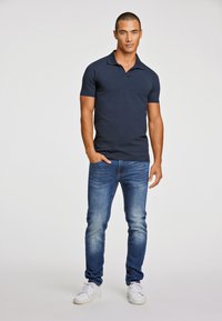 Camisa polo de color azul marino con mangas cortas, combinada con jeans de color azul claro y zapatillas blancas. Textura suave y ajuste casual.