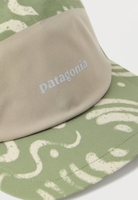 Μπεζ και πράσινο καπέλο με αφηρημένα λευκά σχέδια και το λογότυπο "patagonia" εκτυπωμένο σε άσπρο στο μπροστινό πάνελ.