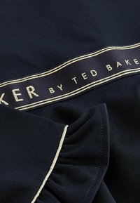 Námořnický vrchní díl z látky se zvonovými rukávy, zlatě lemovanou logovou páskou s textem "Ted Baker" a hladkým povrchem.