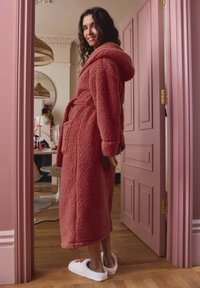 Cozy pink fleece robe with a hood, featuring two front pockets and a tie belt, worn with soft white slippers adorned with flowers.