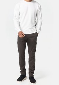 Sudadera blanca de manga larga con cuello redondo y estampado negro en el lateral, combinada con pantalones cargo gris oscuro que tienen bolsillos laterales.
