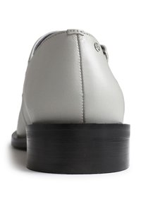 Grauer Lederschuh mit glatter Textur, geschwungenem Design und schwarzem Gummiabsatz. Mit sichtbarer Naht und einem kleinen Logo-Detail.