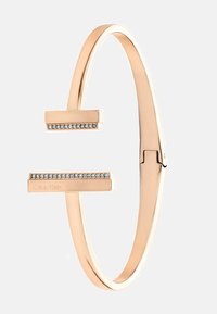 Roosa kuldne bangle käevõru omab minimalistlikku disaini, millel on tasased otsad, millel on ehe rida väikeseid selgeid kristalle ja graveeritud logo.