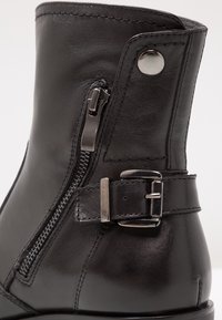 Svart läder ankle boot med sidodragkedja, spänne och texturerad yta. Slät yta med kontrasterande sömmar.