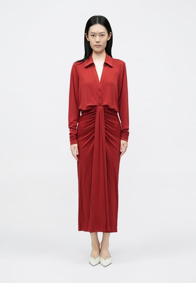 Abito in maglia rossa con collo a camicia abbottonato, maniche lunghe e dettaglio arricciato sul davanti. Presenta un design fluente e una lunghezza a metà polpaccio.