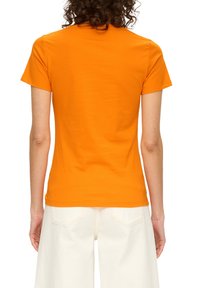T-shirt ajusté à manches courtes en coton orange vif, avec un col rond et une texture douce, associé à un pantalon blanc taille haute.