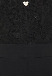 Top nero con design in pizzo testurizzato caratterizzato da motivi floreali. Include una vita nera solida e un dettaglio a forma di cuore.