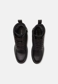 Bottines en cuir noir avec lacets, texture lisse, bout arrondi et tirant. Intérieur doublé d'un tissu doux pour le confort.