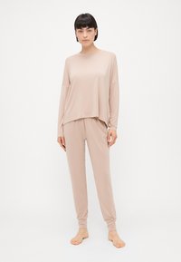 Lagani, meki, bež loungewear set s majicom dugih rukava širokog kroja i suženim hlačama, s opuštenim, minimalističkim dizajnom.