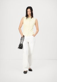 Light yellow, sleeveless top with buttons in front, paired with white wide-leg pants and black slip-on shoes. Holds a small black handbag.