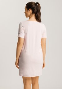 Vaaleanpunainen, lyhythihainen mekko, jossa on pyöreä kaula-aukko, sileä rakenne, polvimittainen leikkaus ja sivuhalkiot liikkumisen helpottamiseksi.