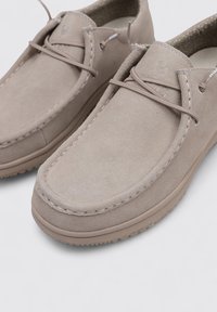 Scarpe in suede beige con una texture liscia, punta rotonda e design minimalista. Presentano una chiusura con lacci e dettagli di cucitura sottili.