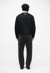 Chaqueta de mezclilla negra con un cuello de borreguito blanco, combinada con pantalones sueltos de color marrón oscuro. Los detalles visibles incluyen botones y costuras.
