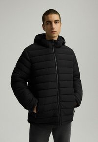 Czarna kurtka puchowa z poziomym przeszyciem, przymocowanym kapturem i zapięciem na zamek. Materiał wydaje się gładki i lekki. Akcenty z teksturowanej tkaniny.