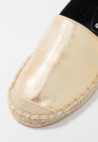 Espadrille métallique doré avec une surface lisse, semelle en jute, bordure tissée et bout arrondi. L'intérieur est doté d'un doublure en tissu noir.