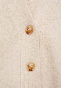 Cardigan en laine beige avec un col en V, doté de deux boutons ronds marbrés et d'une surface texturée. Détails subtils côtelés le long des bords.