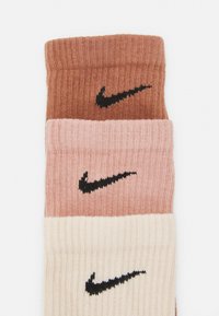 Calze Nike in tre colori: marrone scuro, rosa chiaro e crema. Presentano una texture a coste e il logo Nike nero su ciascuna.