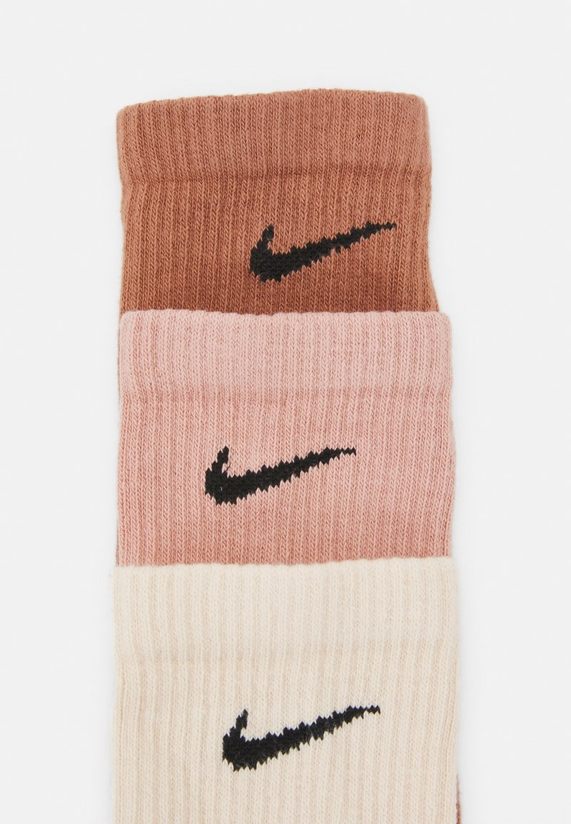 Sosete Nike în trei culori: maro închis, roz deschis și crem. Prezintă o textură riblată și un logo Nike negru pe fiecare.