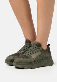 Sneaker atletiche verdi caratterizzate da un mix di materiali in suede e mesh, suola spessa, cuciture dettagliate e colletto imbottito.
